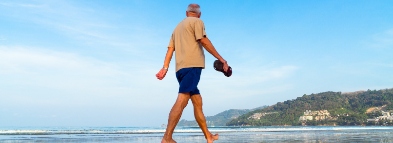 Elderly man walks on beach.